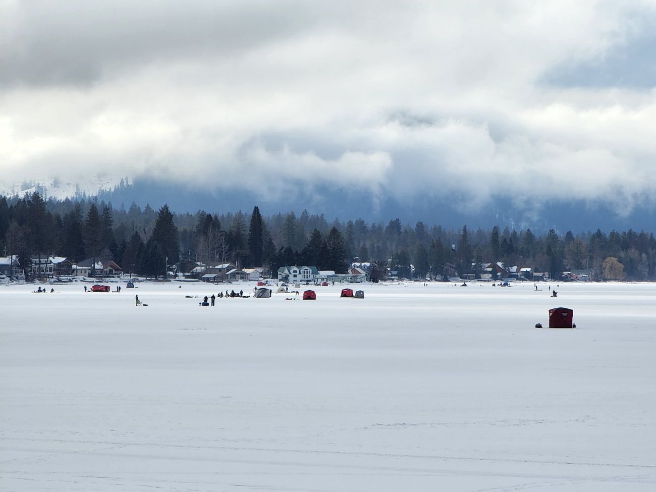 Ice fishing shelters on the frozen lake beneath low clouds
